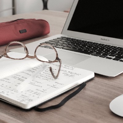 block notes in primo piano con occhiali appoggiati su scrivania con pc portatile